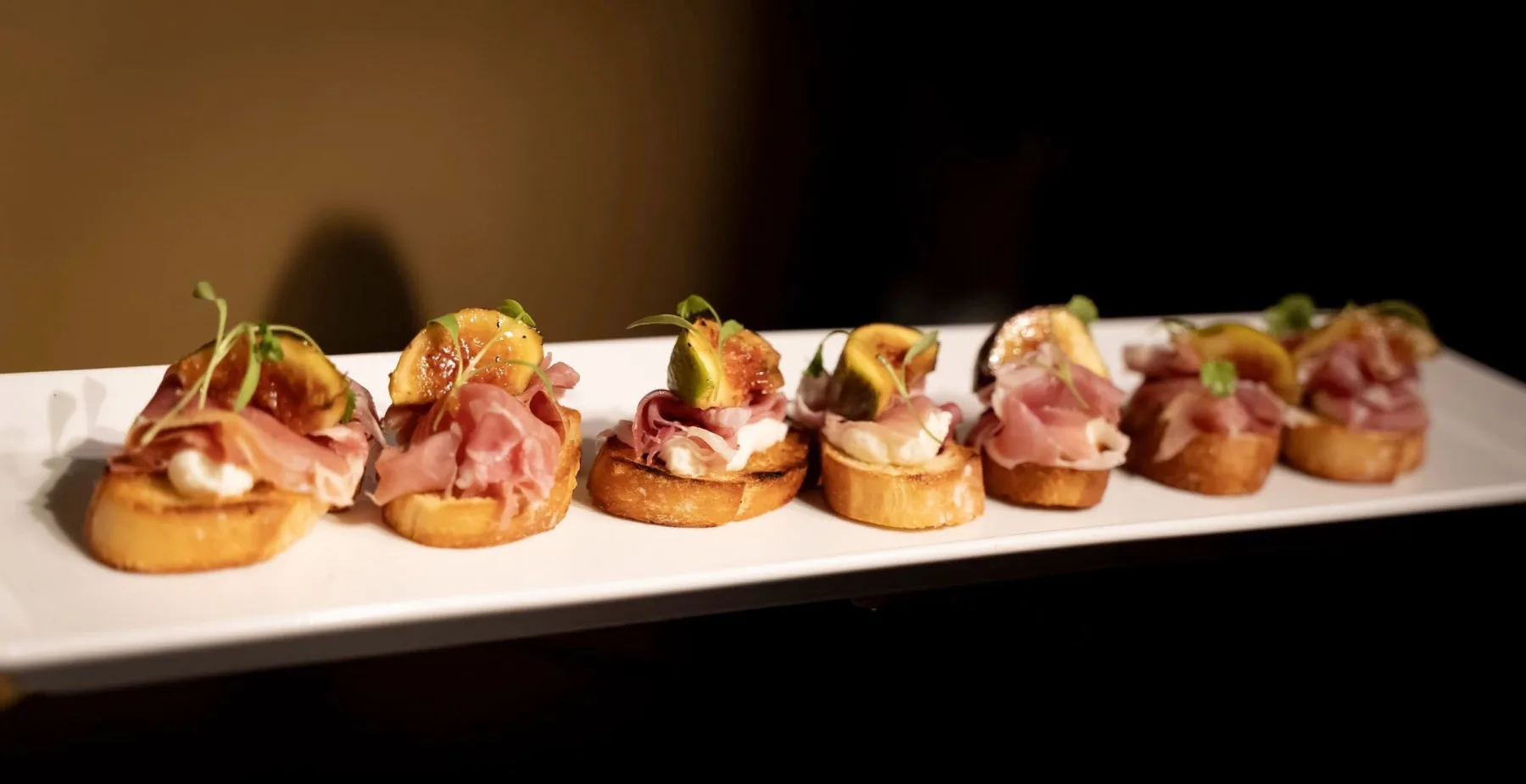 A tray of prosciutto and fig crostini ready for passed service